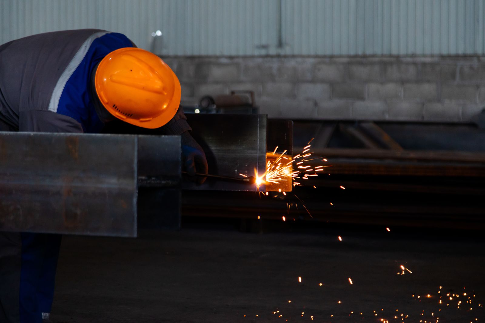 Welder in an orange hard hat welding a steel beam in a fabrication workshop